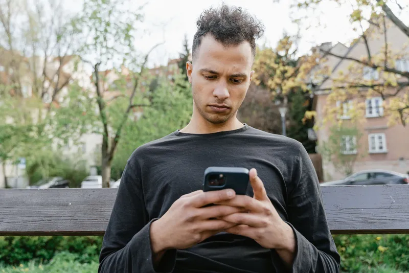 Dışarıda başı öne eğik şekilde telefonuna bakan genç adam
